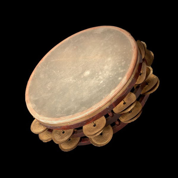 A brown tambourine, also known as a Schellentrommel or Basque drum, with a light-colored drumhead and brass jingles against a black background.