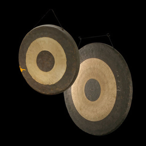 Two dark gongs hanging in front of a black background, one slightly smaller and higher than the other. Both have large light-colored rings around their dark centers.